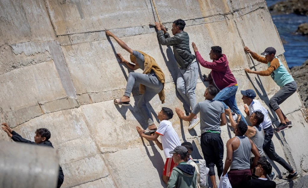 Des migrants escaladent une digue dans la ville de Fnideq après avoir tenté de traverser la frontière entre le Maroc et l'enclave nord-africaine espagnole de Ceuta le 19 mai 2021. FADEL SENNA / AFP