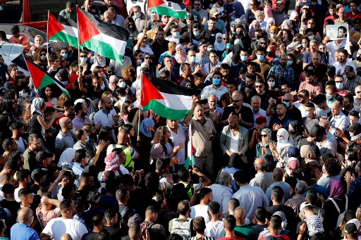 Des Palestiniens lèvent des pancartes et des drapeaux nationaux alors qu'ils se rassemblent dans la ville de Ramallah en Cisjordanie occupée, le 26 juin 2021, pour protester contre la mort du militant des droits humains Nizar Banat (Photo, AFP)