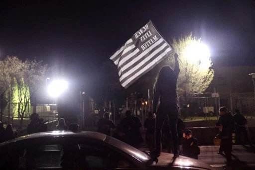 Un manifestant se tient sur une voiture et brandit un drapeau lors d'une manifestation devant le poste de police de Brooklyn Center, le 17 avril 2021 à Brooklyn Center, Minnesota (Photo, AFP)