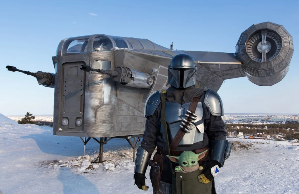 Un homme portant un costume du protagoniste de StarWars Din Djarin pose devant une réplique géante du Razor Crest (AFP)