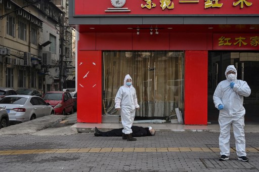 Cette photo prise le 30 janvier 2020 montre des fonctionnaires en tenue de protection vérifiant un homme âgé portant un masque facial qui s'est effondré et est décédé dans une rue près d'un hôpital de Wuhan. (Hector Retamal/AFP)