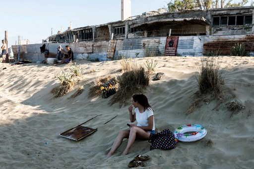 Une femme est assise sur le sable d'une plage de la zone clôturée de Varosha, dans la ville de Famagouste, dans la République turque autoproclamée de Chypre du Nord (RTCN) de l'île méditerranéenne divisée de Chypre, le 19 juin 2021. (Iakovos Hatzistavrou/AFP)