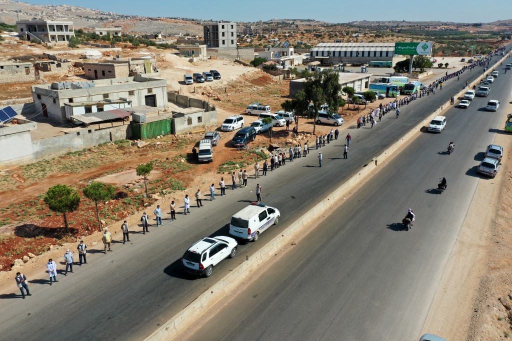 Une chaîne humaine est formée par des travailleurs de la société civile, de l'aide humanitaire et des services médicaux et de secours lors d'une veillée appelant au maintien d'une résolution de l'ONU autorisant le passage de l'aide humanitaire dans la province d'Idlib, au nord-ouest de la Syrie, tenue par les rebelles, via le poste frontière de Bab al-Hawa avec la Turquie, près de Bab al-Hawa, le long de l'autoroute qui la relie à la ville d'Idlib, le 2 juillet 2021. (Omar HAJ KADOUR / AFP)