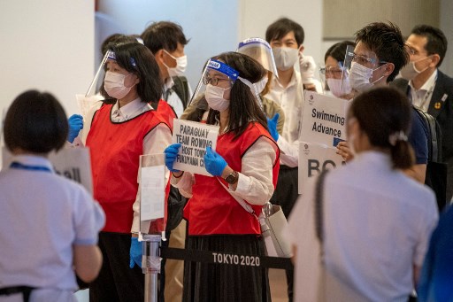 Le personnel d'accueil des délégations olympiques tient des pancartes dans le hall des arrivées de l'aéroport international de Tokyo le 8 juillet 2021, avant les Jeux olympiques. (Kazuhiro Nogi/AFP)