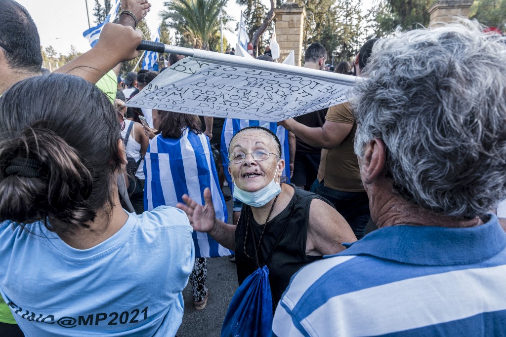 Une manifestante opposée aux restrictions sanitaires, aux côté de protestataires dont certains sont drapés dans le drapeau grec, devant le palais présidentiel de Nicosie le 18 juillet 2021 Iakovos Hatzistavrou / AFP