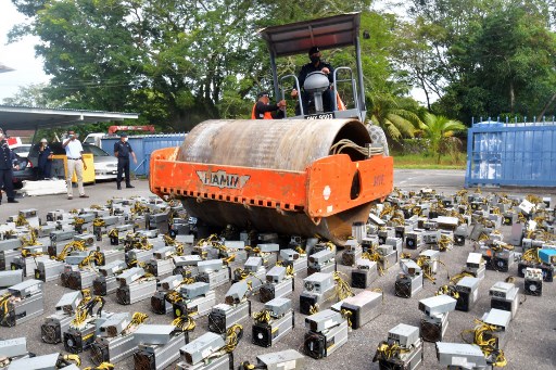 Cette photo prise le 16 juillet 2021 montre la police au siège de la police du district de Miri surveillant la destruction de machines d'extraction de bitcoins écrasées au rouleau compresseur, dans la ville malaisienne de Miri à Bornéo. (Dennis Wong / Avec l'aimable autorisation de Dennis Wong / AFP)