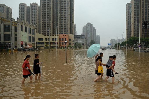 Des gens traversent une artère inondée à la suite de fortes pluies qui ont provoqué des inondations et coûté la vie à au moins 33 personnes plus tôt dans la semaine, dans la ville de Zhengzhou, dans la province chinoise du Henan, le 23 juillet 2021. (Noël Celis/AFP)