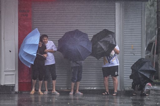 Des gens cherchent à s'abriter de la pluie et du vent le long d'une rue de Ningbo le 25 juillet 2021, alors que le typhon In-Fa frappe la côte est de la Chine. (Hector Retamal/AFP)