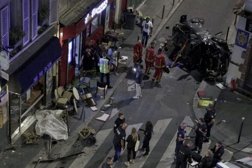Des pompiers à l’œuvre alors que des policiers français montent la garde après qu'une voiture est entrée dans la terrasse du café "Bar aux sports", au croisement des rues Sauffroy et Guy Moquet, dans le nord-ouest de Paris, le 29 juillet 2021.(Geoffroy Van Der Hasselt/ AFP)