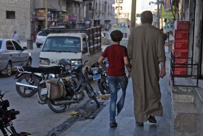 Un syrien déplacé, Mustafa Shaaban Abu Khalil, marche aux côtés de son fils qui a perdu une jambe à cause d'un bombardement, dans une rue de la ville rebelle d'al-Bab, au nord-ouest d'Alep, dans le nord de la Syrie, le 23 juin 2021. (AFP)