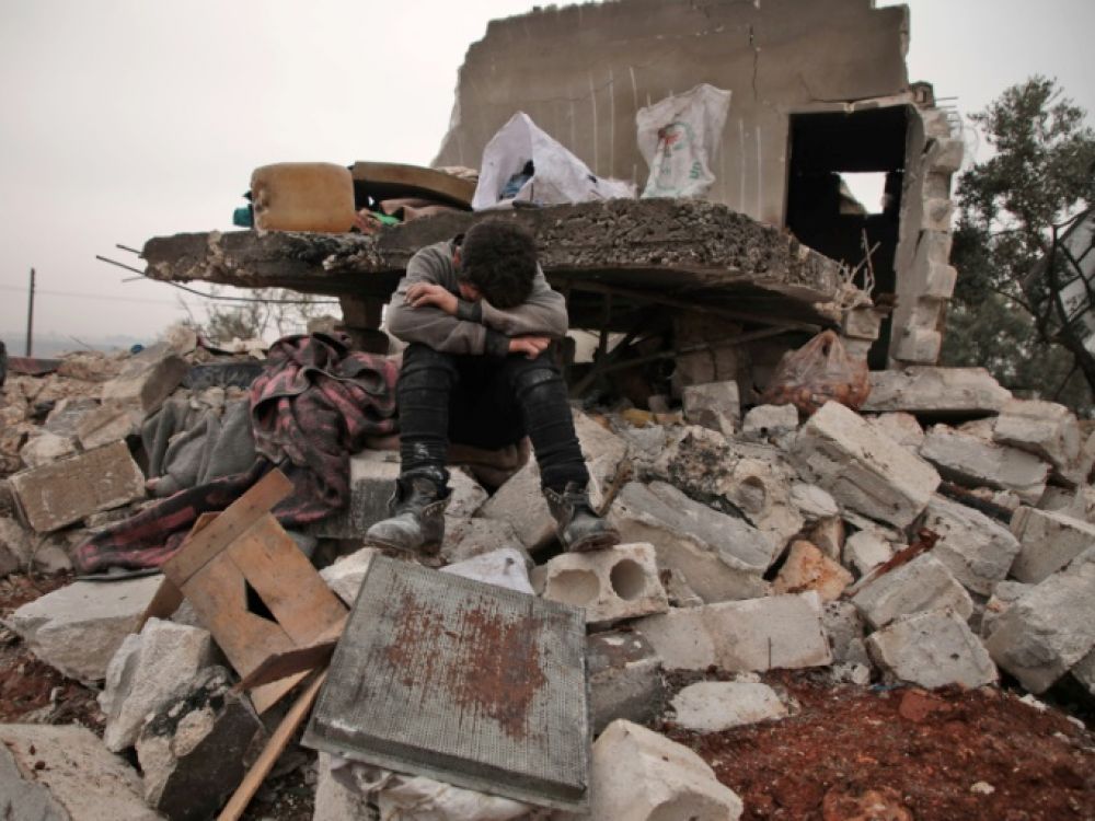 Un enfant syrien pleure, assis sur les décombres de la maison où il vivait avec sa famille déplacée dans le village de Kafr Taal, dans la province d'Alep, après des bombardements du régime, le 20 janvier 2020. Photo d'archives AFP