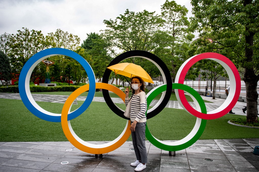 Une femme pose avec les anneaux olympiques devant le Musée olympique du Japon à Tokyo, le 8 juillet 2021 (AFP)