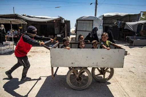 Un jeune homme pousse une charrette avec des enfants assis à l'intérieur du camp kurde d'al-Hol, qui abrite des proches de combattants présumés du groupe État islamique (EI), dans le gouvernorat de Hasakeh, dans le nord-est de la Syrie, le 23 juin 2021. (Delil Souleiman /AFP)
