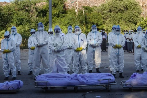 Des volontaires portant des équipements de protection individuelle (EPI) prient devant les corps de personnes décédées du coronavirus Covid-19 lors de leurs funérailles dans un cimetière de Mandalay le 14 juillet 2021.(STR / AFP)