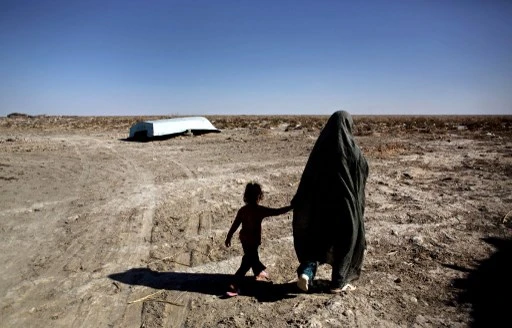 Une Iranienne passe avec sa fille devant un bateau abandonné dans le village de Sikh Sar dans la zone humide de Hamoon, près de la ville de Zabol, dans la province sud-est du Sistan-Balouchistan, à la frontière de l'Afghanistan, le 2 février 2015. (Behrouz Mehri/AFP)
