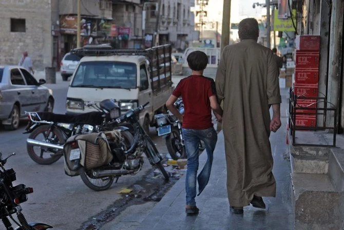 Un syrien déplacé, Mustafa Shaaban Abu Khalil, marche aux côtés de son fils qui a perdu une jambe à cause d'un bombardement, dans une rue de la ville rebelle d'al-Bab, au nord-ouest d'Alep, dans le nord de la Syrie, le 23 juin 2021. (AFP)