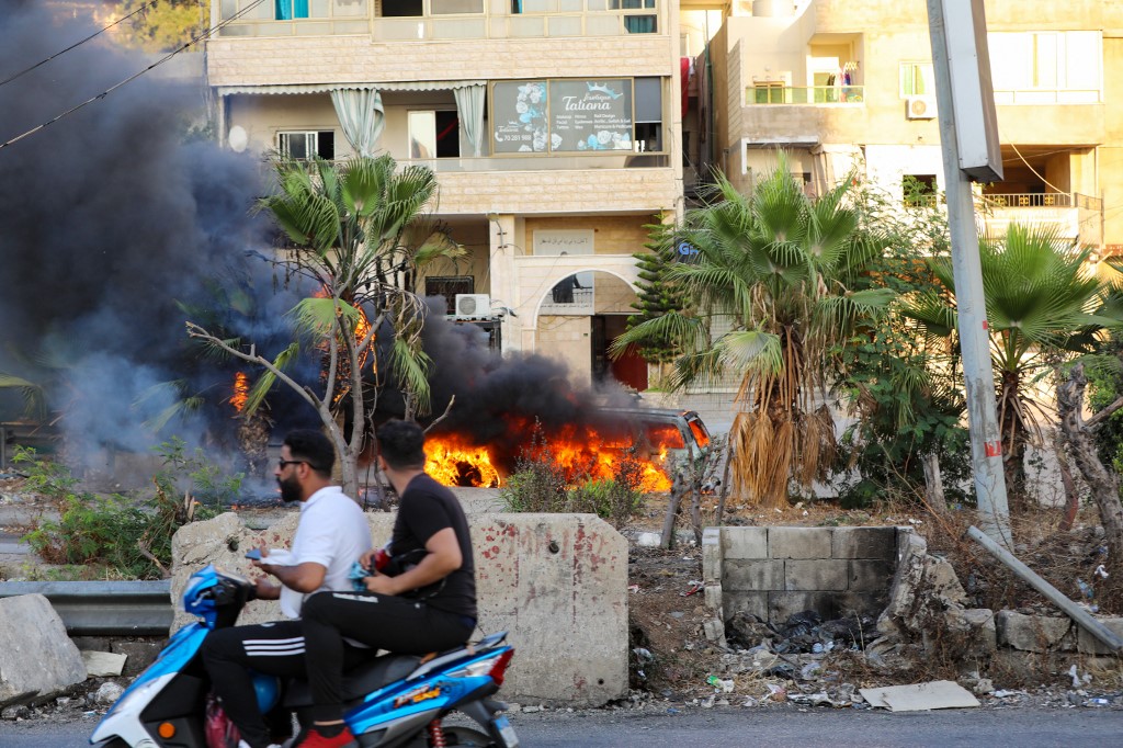Des Libanais passent à moto devant un véhicule à la suite d'affrontements dans la région de Khalde, au sud de la capitale, le 1er août 2021. (AFP)