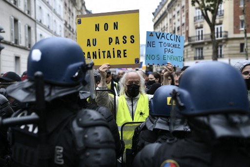 Un manifestant tient des pancartes indiquant "Non au laissez-passer sanitaire" et "Vaccin : éloignez-vous de nos enfants" devant les forces anti-émeutes lors d'une manifestation, près du pont de Neuilly le 7 août 2021. (Stephane de Sakutin / AFP)