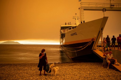 Une femme avec son chien à côté d'un ferry dans le port du village de Pefki, le 8 août 2021lors d'un incendie de forêt dans le village de Pefki sur l'île d'Eubée (Eubée), la deuxième plus grande île grecque, où des centaines d’habitations ont été détruites par le feu. (Angelos Tzortzinis / AFP)