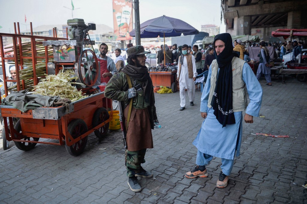 Un combattant taliban se tient près d'un kiosque vendant du jus de canne à sucre dans une zone de marché, afflué avec des Afghans locaux dans la région de Kote Sangi à Kaboul le 17 août 2021, après que les talibans ont pris le contrôle de la capitale à la suite de l'effondrement du gouvernement afghan. (AFP)