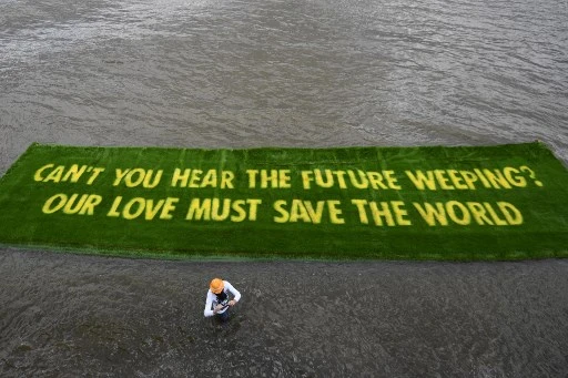 Un message sur un tapis d'herbe vive flotte sur la Tamise dans le centre de Londres le 25 juin 2021. Il invite les gouvernements à agir rapidement, dans la perspective de la COP26. (Daniel Leal-Olivas/AFP)