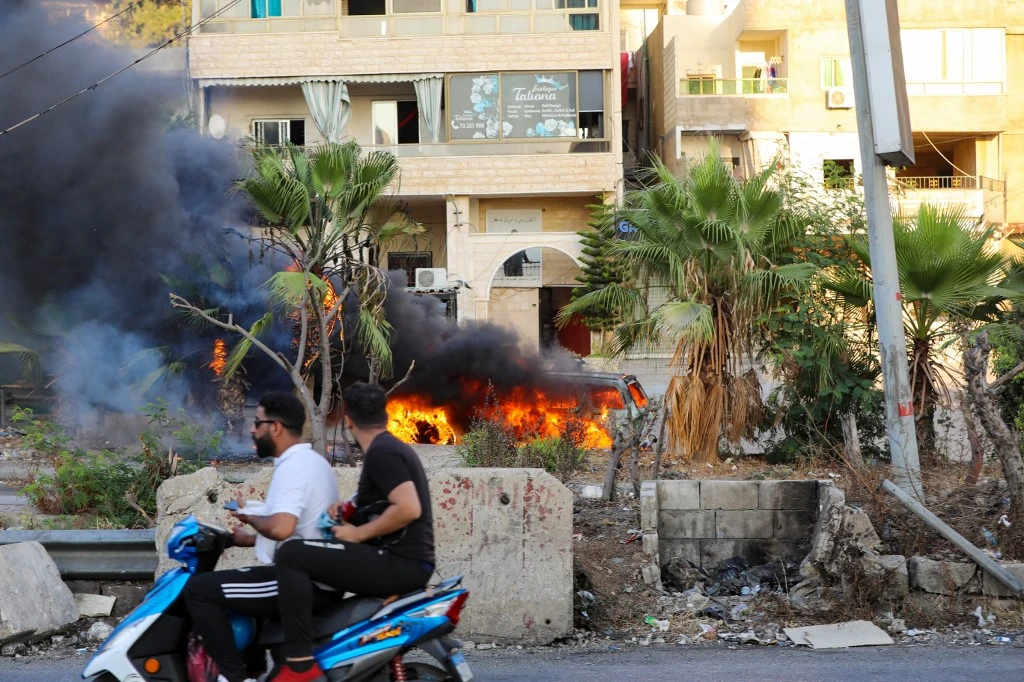 Des Libanais passent à moto devant un véhicule à la suite d'affrontements dans la région de Khalde, au sud de la capitale, le 1er août 2021. (AFP)
