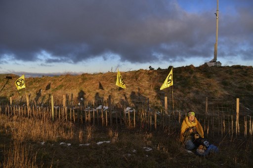 Un militant du groupe d'action climatique Extinction Rebellion est assis sur un bord d'herbe alors que des militants locaux bloquent l'entrée du site de la mine de charbon à ciel ouvert Bradley près du village de Leadgate, comté de Durham, au nord-est de l'Angleterre le 26 février 2020. (Paul Ellis/ AFP)