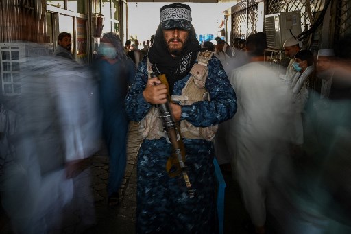 Un combattant taliban monte la garde alors que des gens passent devant lui sur un marché avec des magasins de change à Kaboul le 5 septembre 2021. (Aamir Qureshi/AFP)