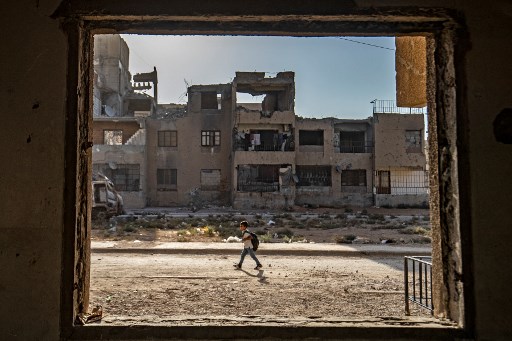Un écolier syrien se rend à l'école à pied devant des bâtiments endommagés de la ville de Raqqa, dans le nord du pays, le 23 septembre 2021. (Delil Souleiman/AFP)