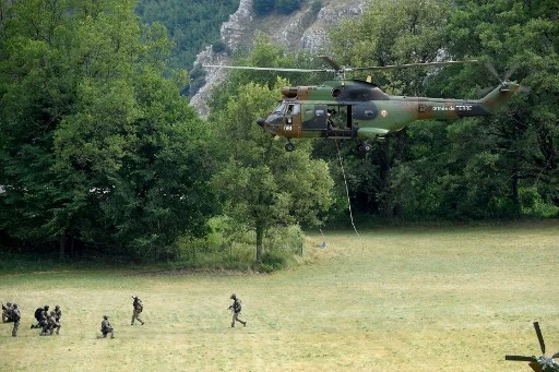 Des membres du Groupe d'intervention de la gendarmerie nationale (GIGN) se tiennent dans un champ alors qu'un hélicoptère Puma de l'Armée de Terre française atterrit à Gréolières, dans le sud-est de la France, le 19 juillet 2021 (Photo, AFP)