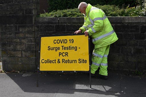 Un travailleur présente un panneau pour un site de test Covid-19 PCR et un centre de vaccination, à l'Église réformée unie de Blackburn, dans le nord-ouest de l'Angleterre, le 19 mai 2021.(Oli Écharpe/AFP)