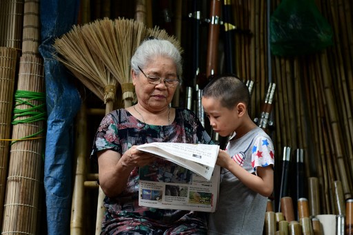 Une femme lit un journal avec un garçon devant son magasin de bambou à Hanoï le 5 juillet 2021. (Nhac Nguyen / AFP)