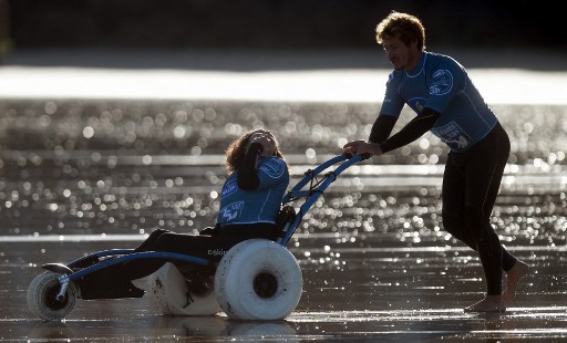 Une personne handicapée est poussée sur un fauteuil roulant avant une session de Handi-Surf avec un professeur d'une école de surf locale sur la plage de la ville d'Hendaye au Pays basque français le 8 octobre 2021. (Gaizka Iroz/AFP)