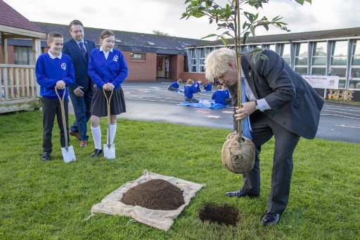 Le Premier ministre britannique Boris Johnson plante un arbre avec l'aide de jeunes élèves lors d'une visite à l'école primaire intégrée Crumlin dans le comté d'Antrim, en Irlande du Nord, le 21 octobre 2021, après avoir assisté à un service pour marquer le centenaire de la création de l'Irlande du Nord après la partition de l'Irlande en mai 1921. (Paul Faith/Pool/AFP)