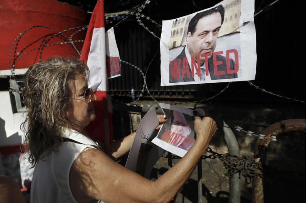 Une militante accroche des photos de l’ancien Premier ministre libanais, Hassan Diab, et de l’ancien ministre des Travaux publics, Youssef Fenianos, tous deux accusés de négligence ayant entraîné la mort, dans le cadre de l’enquête sur l’explosion du port de Beyrouth. (AP)