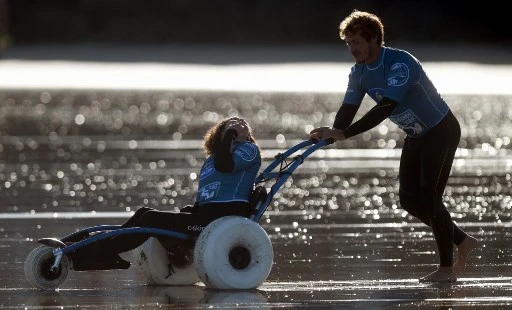 Une personne handicapée est poussée sur un fauteuil roulant avant une session de Handi-Surf avec un professeur d'une école de surf locale sur la plage de la ville d'Hendaye au Pays basque français le 8 octobre 2021. (Gaizka Iroz/AFP)