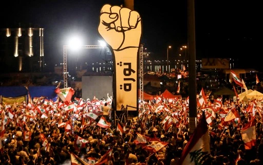 Dans cette photo d'archive prise le 10 novembre 2019, des manifestants libanais brandissent des drapeaux nationaux lors des manifestations antigouvernementales en cours au cœur de Beyrouth. Deux ans après qu'un mouvement de protestation aujourd'hui disparu a secoué le Liban, les militants de l'opposition espèrent que les sondages parlementaires remettront en cause la mainmise de l'élite dirigeante sur le pays. (Anwar Amro / AFP)