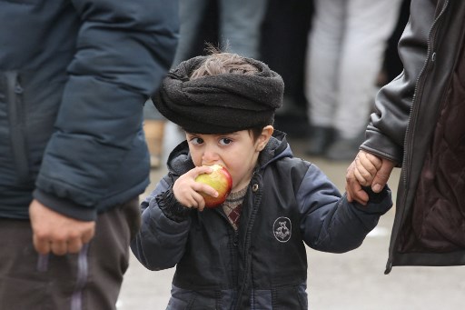 Un enfant migrant mange une pomme à l'extérieur du centre de transport et de logistique près du poste frontière de Bruzgi à la frontière biélorusse-polonaise dans la région de Grodno le 19 novembre 2021. (Leonid Shcheglov/Belta/AFP)