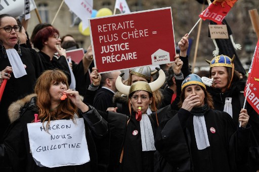 Des manifestants brandissent des pancartes indiquant «Macron nous culpabilise» (à gauche) et «Retraite plus chère = justice précaire» (à droite) lors d'une manifestation convoquée par le collectif «SOS Retraites» rassemblant avocats, médecins, infirmiers, pilotes et autres travailleurs indépendants, pour protester contre la réforme du système des retraites par le gouvernement français, le 3 février 2020, à Paris. (Christophe Archambault / AFP)