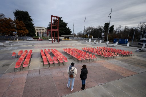 Des militants devant une installation de chaises formant le nombre de 10000, nombre de personnes qui meurent actuellement de Covid-19 chaque jour, lors d'une manifestation en faveur d'un accord visant à renoncer à la protection des brevets pour les vaccins Covid-19 le 30 novembre 2021 à Genève. (Fabrice Coffrini/AFP)