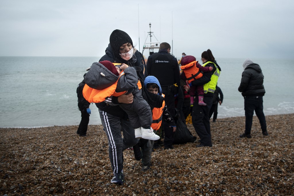 Une migrante porte ses enfants après avoir été aidée par la RNLI (Royal National Lifeboat Institution) sur une plage de Dungeness, sur la côte sud-est de l'Angleterre, le 24 novembre 2021 (Ben STANSALL / AFP)