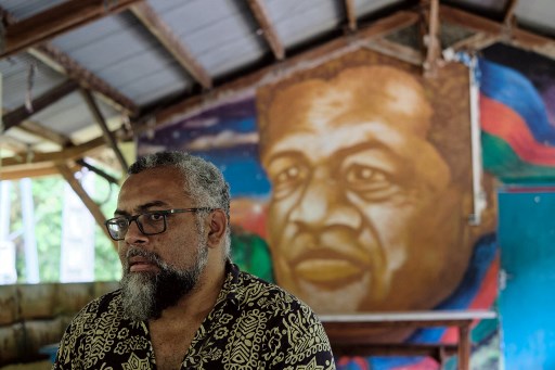 Emmanuel Tjibaou, le fils du leader indépendantiste kanak Jean-Marie Tjibaou, pose devant un portrait mural de son défunt père dans la tribu de la maison Tiendanite, à Hienghène, le 19 décembre 2021. (Théo Rouby / AFP)