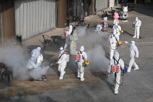 Des membres du personnel portant un équipement de protection individuelle (EPI) vaporisent du désinfectant à l'extérieur d'un centre commercial à Xi'an, dans la province du Shaanxi (nord de la Chine), le 11 janvier 2022. (STR/AFP)