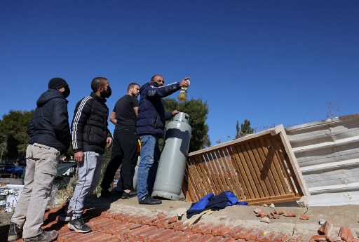 Des Palestiniens tiennent un réservoir d'essence sur le toit d'une maison alors que la police israélienne se prépare à expulser une famille du même bâtiment le 17 janvier 2022 dans le quartier est de Sheikh Jarrah à Jérusalem. (Ahmad Gharabli / AFP)