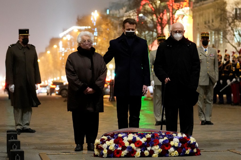 Le président français Emmanuel Macron flanqué de la survivante du camp de concentration d'Auschwitz Esther Senot et de la survivante du camp de concentration de Bergen-Belsen Victor Perahia au garde-à-vous sur la Tombe du Soldat inconnu sous l'Arc de Triomphe lors d'une cérémonie pour marquer la Journée internationale de commémoration de la Shoah, le 27 janvier 2022 à Paris. (AFP)