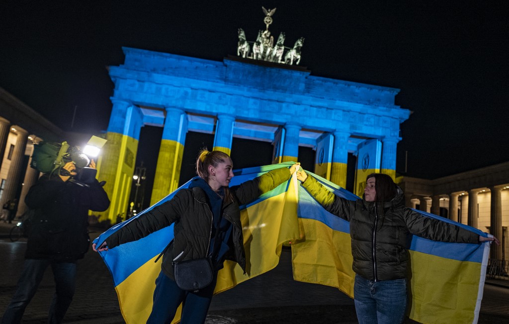 Deux Ukrainiennes posent avec le drapeau de leur pays devant la célèbre porte de Brandebourg alors qu'elle est illuminée aux couleurs du drapeau ukrainien au milieu des tensions russo-occidentales sur l'Ukraine à Berlin le 23 février 2022 (AFP)