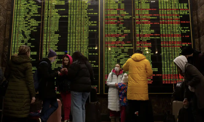 Des personnes se tiennent devant l'horaire des trains à la gare centrale alors qu'ils tentent de quitter Kiev. (Reuters)