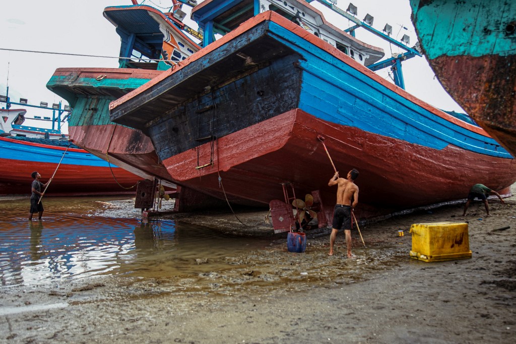 Des ouvriers rénovant des bateaux de pêche traditionnels sur la côte de Lhokseumawe, sur l'île de Sumatra, en Indonésie. (AFP). 