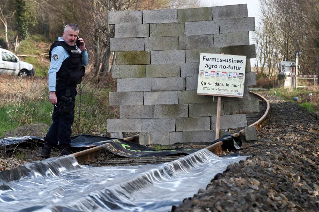 Un gendarme se tient à côté d'un mur construit par des membres du collectif "Bretagne contre les fermes usines" pour arrêter un train sur la voie ferrée reliant l'usine Sanders Bretagne à Saint-Gerand, près de Pontivy, le 19 mars 2022. (AFP).