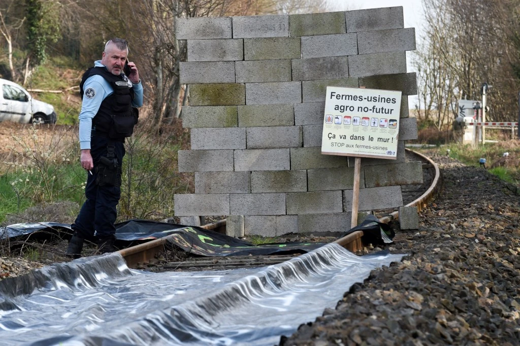 Un gendarme se tient à côté d'un mur construit par des membres du collectif "Bretagne contre les fermes usines" pour arrêter un train sur la voie ferrée reliant l'usine Sanders Bretagne à Saint-Gerand, près de Pontivy, le 19 mars 2022. (AFP).